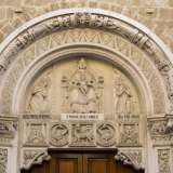 Due grifoni alati sorreggono da entrambi i lati l'arco superiore, a sua volta decorato con bassorilievi di angeli e uomini nell'atto di preghiera. Infine nel lunettone sopra la porta si trova la Vergine seduta in trono col bambino attorniata anch'ella da angeli